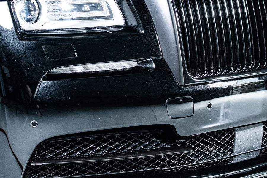 Close-up of a luxury black car's front grille and headlight detailing, showcasing sleek design and craftsmanship.