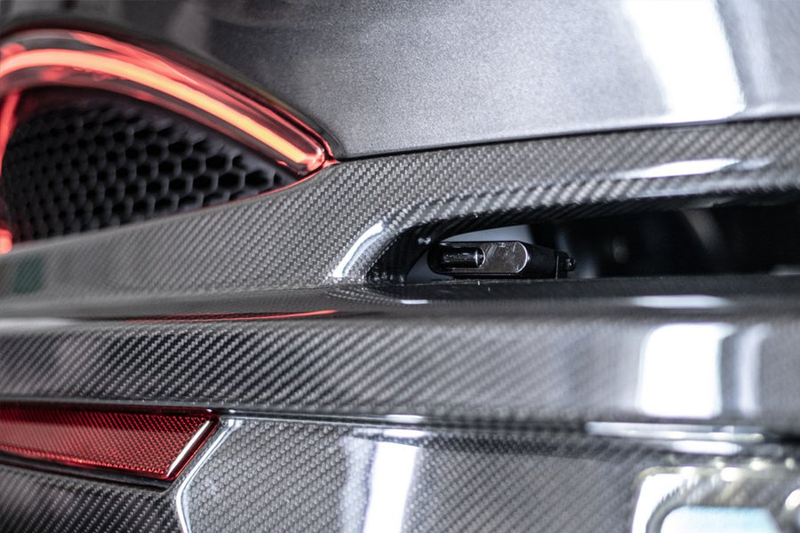 Close-up of carbon fiber detailing on a luxury car rear bumper with an exhaust and red tail light.
