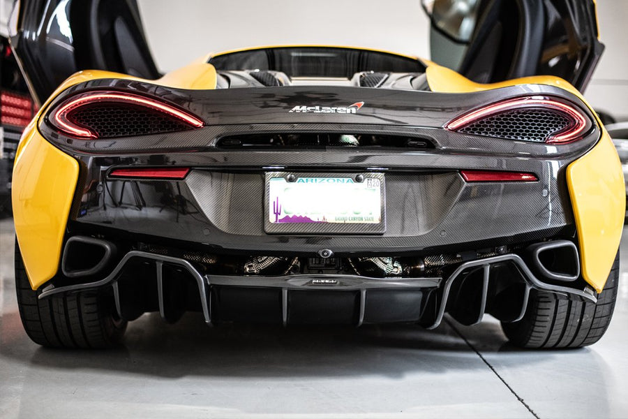 Rear view of a yellow sports car with black detailing and open doors in a garage setting.