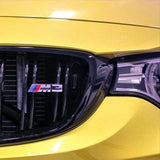 Close-up of the front grille and headlight of a yellow BMW M3 with the M3 emblem.